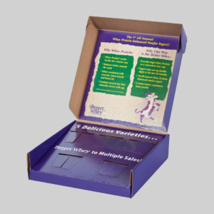 An open cardboard display box with a purple and brown design. The inside lid features graphics promoting whey protein nougat squares, with sections titled "Why Whey Protein" and "Why Our Way is Better Whey". The base is purple, divided into compartments, making the packaging both attractive and functional.