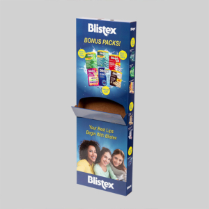 The display box for Blistex lip balm bonus packs boasts vibrant graphics on the upper section, showcasing various Blistex products and an image of smiling people at the bottom. The blue package features the slogan "Your Best Lips Begin With Blistex" prominently. The box is open for easy access.