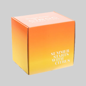 A cube-shaped box with a gradient from orange to yellow, showcasing stunning graphics. Text on one side reads "Summer Starts With Citrus" in white. The top features "Cocktail Courier" and "CÎROC," also in white. This vibrant packaging is set against a plain gray background.