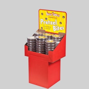 A red display stand filled with Aft Tapple Confections Pretzel Bites features sharp graphics. The sign at the top prominently displays the product name "Pretzel Bites" in large font, with "chocolate covered" written below. Each Pretzel Bite is individually packaged in clear containers.