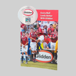 A Glidden paint advertisement features a soccer game with players in red and white jerseys jumping to head the ball. The ad contains the text "Every Wall Looks Better With Glidden" and displays both Glidden and MLS logos on cleverly designed packaging, indicating sponsorship.