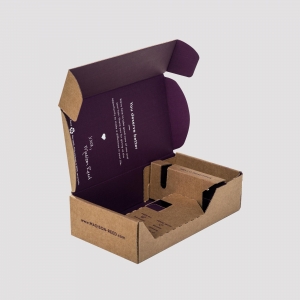 A partially opened cardboard box with the lid lifted, revealing a purple interior and sharp graphics inside. The package contains compartments for organization and has the website "MADISON-REED.com" printed on the exterior.