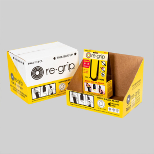 The image shows two Re-Grip branded cardboard boxes. One box is closed, and the other is open, revealing its contents: a re-grip tool. Both boxes are primarily yellow with black and red text and sharp graphics demonstrating the tool's use, showcasing impressive packaging design.