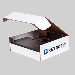 A white cardboard box with a partially open lid reveals a black interior containing a custom cut-out section. The front of the package displays the text "#RETROFIT" accompanied by a logo featuring sharp graphics with a hashtag symbol. The background is solid light gray.