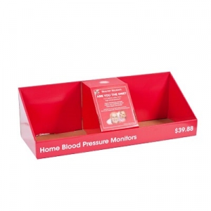 A red retail display box labeled "Home Blood Pressure Monitors," priced at $39.88. The package features three compartments, with the center section displaying a stand holding an info card. Sharp graphics adorn the box, while the other two compartments remain empty.