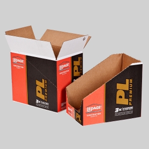 Two cardboard display boxes for LePage PL Premium construction adhesive, partially open and on a gray background. Featuring sharp graphics in red, black, and yellow branding, one box is fully assembled while the other is shown in the folded state, revealing its inner corrugated structure.