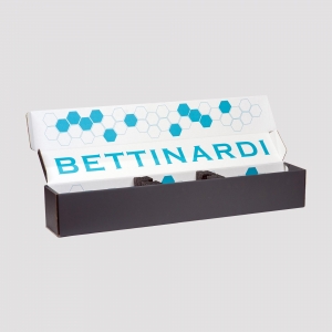 An open rectangular cardboard box displaying the text "Bettinardi" in blue on the inside cover. The inside cover also features a hexagonal pattern in light blue and blue colors. The exterior of the packaging is black.