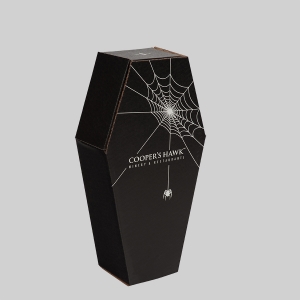 A black, coffin-shaped package features a white cobweb design with a dangling spider. The text "Cooper's Hawk Winery & Restaurants" is printed below the cobweb. The background is plain gray.