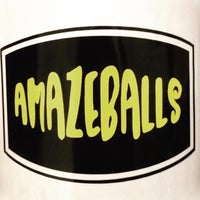 A close-up of a rectangular black sign with a white border, resembling the sharp graphics on smooth packaging. The word "AMAZEBALLS" is written in bold, yellow-green, playful font in the center of the sign.