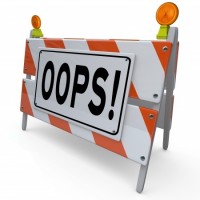 A construction barricade with diagonal orange and white stripes has a large sign that reads "OOPS!" in bold black letters. It looks like someone turned a shipping container into a caution zone. On top of the barricade are two orange warning lights, completing the package of safety.