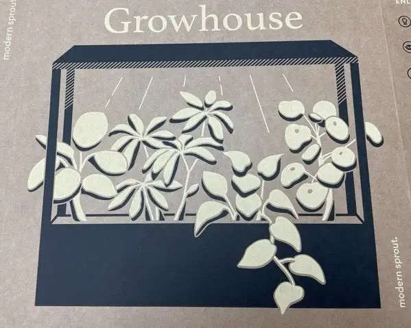 Illustration on a cardboard box showing a rectangular growhouse with a variety of plants inside, labeled "Growhouse." The image, set against sharp graphics, depicts plants growing under grow lights, with some leaves extending outside the structure. Text on the side reads "modern sprout.