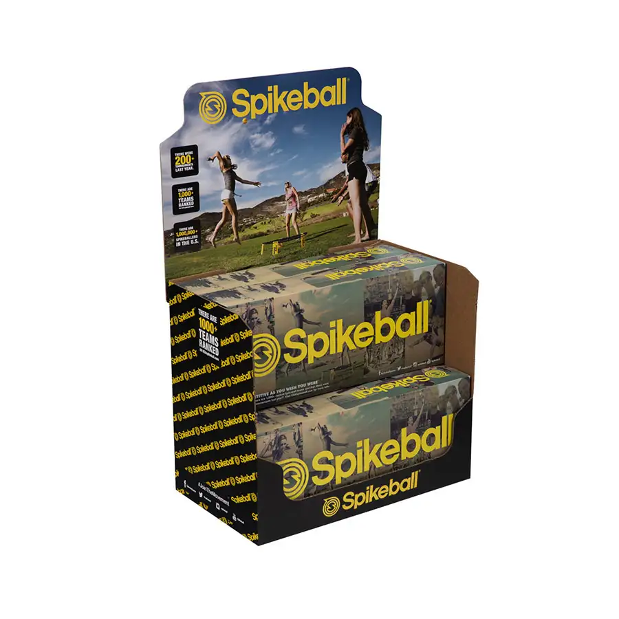 A display box features Spikeball sets, showing two sets with yellow balls in sleek black packaging. The display header has an image of people playing Spikeball outdoors with mountains in the background. The Spikeball logo and text appear prominently in yellow, enhancing the package's appeal.